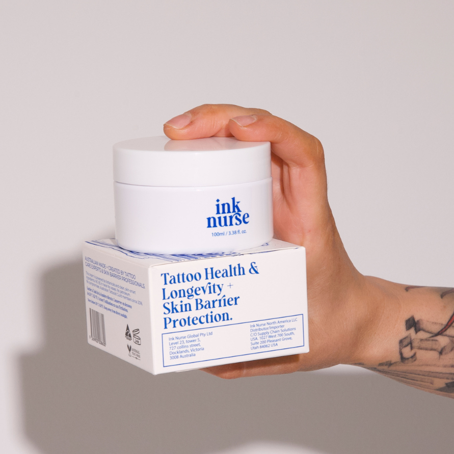 Ink Nurse Remedy Cream 100mL tattoo aftercare jar displayed on its packaging, held by a tattooed hand. Australian-made, petroleum-free skincare.