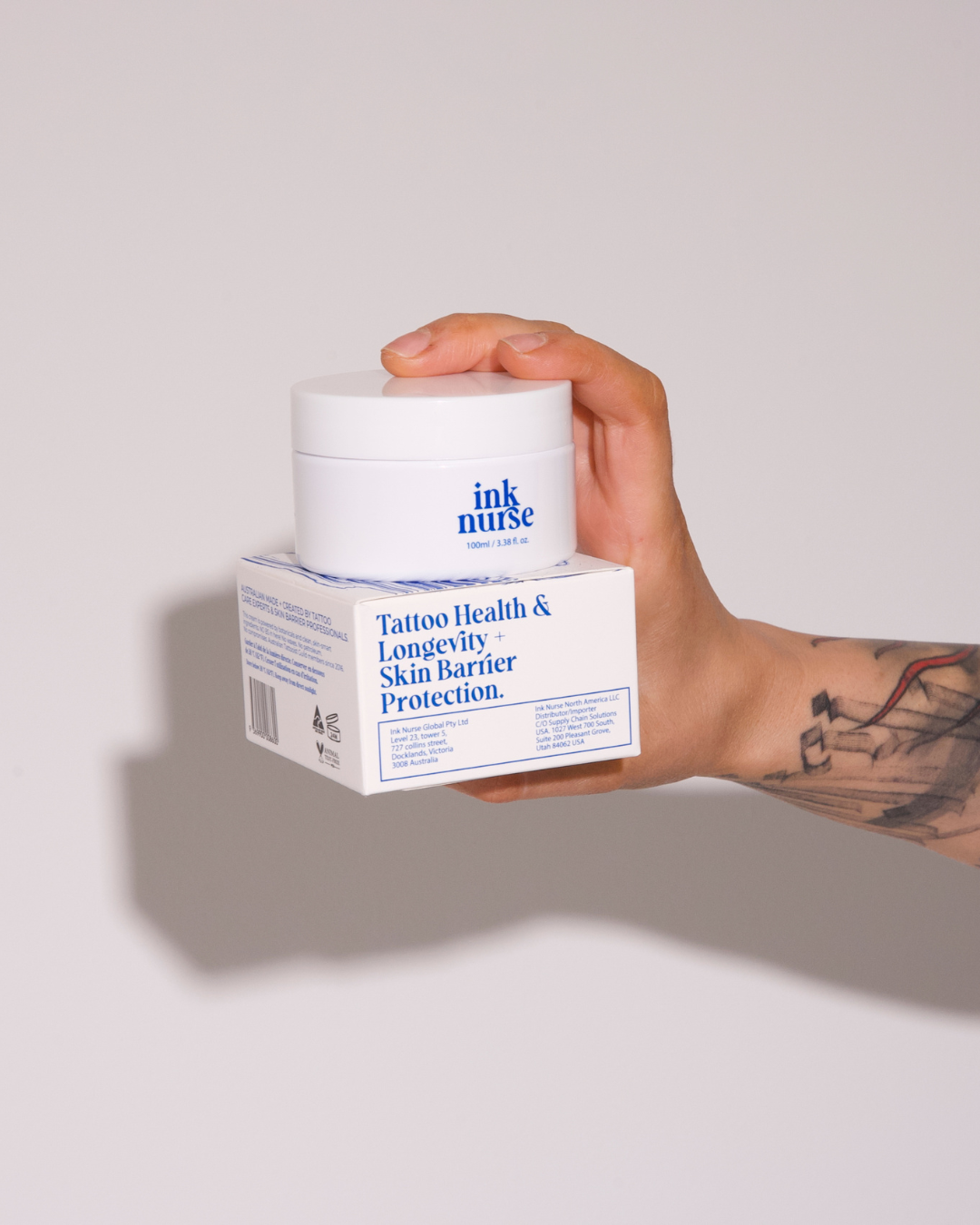 Hand holding a 100ml jar of Ink Nurse tattoo aftercare cream on its box, Australian made, petroleum-free botanical formula