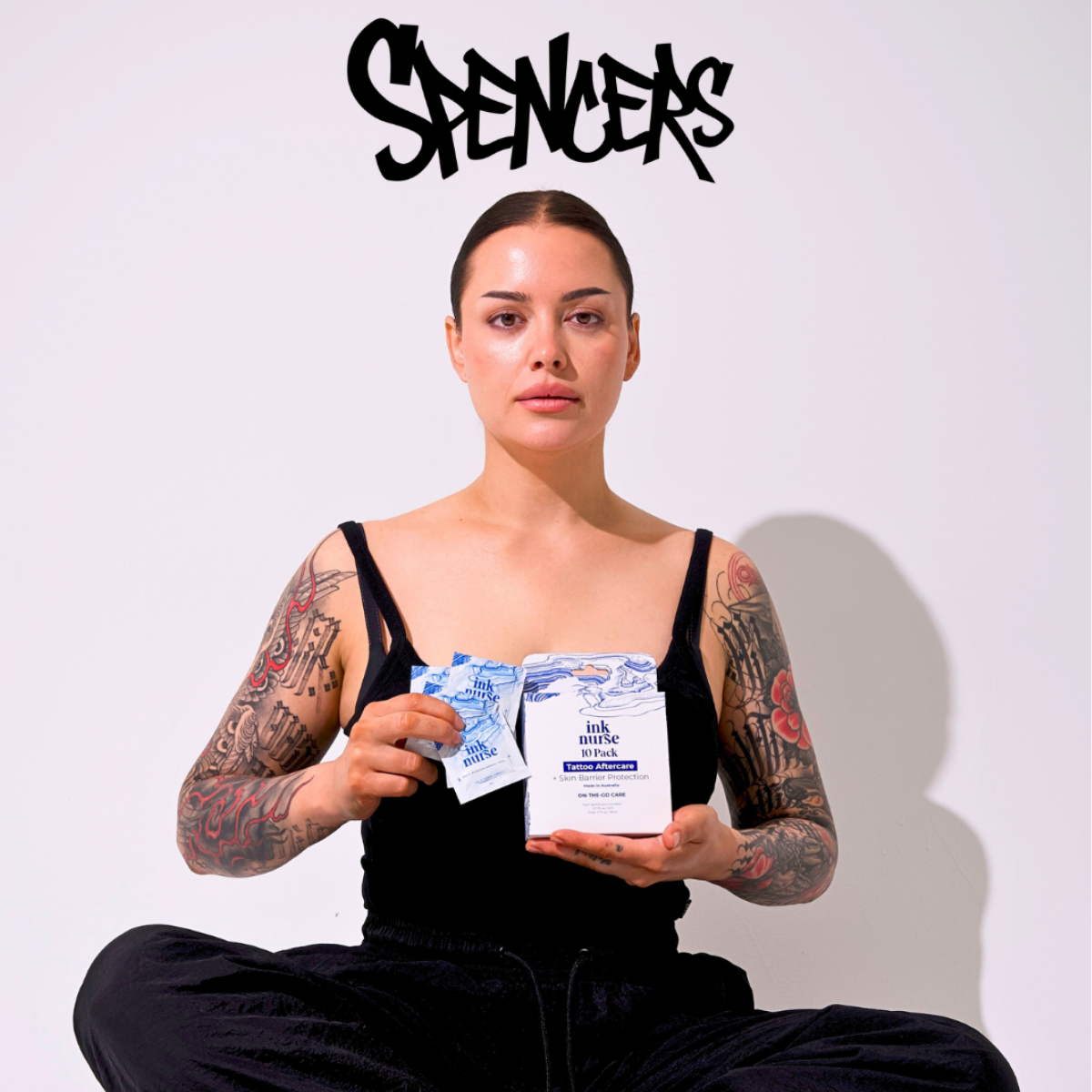 Tattooed model holding Ink Nurse 10-pack sachets and Remedy Cream box, with Spencer's logo above. Australian tattoo aftercare now stocked at Spencer's across the United States. Australia's first and only brand to have US retail presence which Spencer's describe as "Australia's Number 1 Tattoo Aftercare".